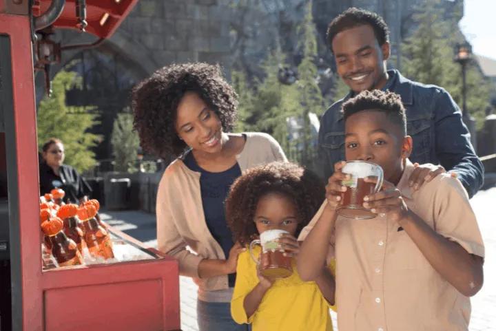A family smiling while drinking Butterbeer next to a beverage cart