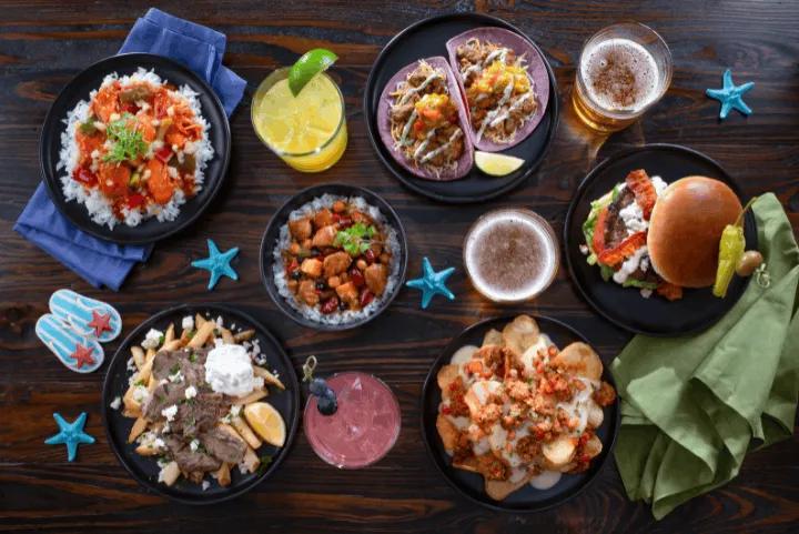 An overhead view of a wooden table displaying various entrees, snacks, and brightly colored cocktails from the Seven Seas Food Festival at SeaWorld Orlando