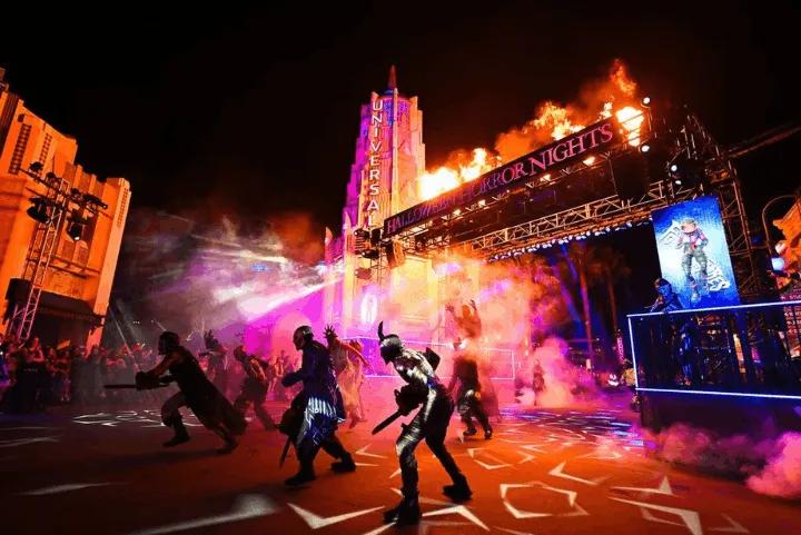 Costumed scareactors roaming a foggy, brightly lit street during Halloween Horror Nights