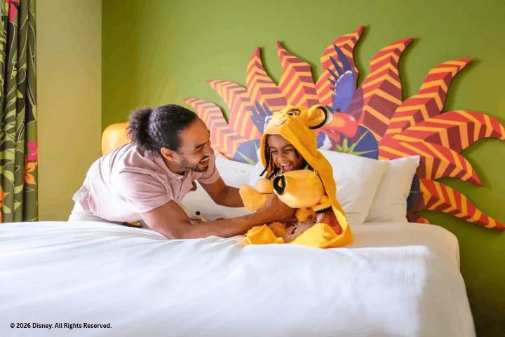 A father and child playing on a bed in a Lion King-themed hotel room