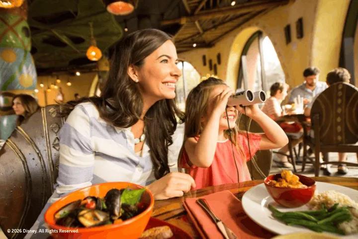 A woman and a young girl dining at a restaurant table, with the girl looking through small binoculars