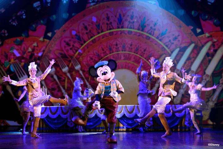 Mickey Mouse performing on stage alongside dancers in colorful costumes