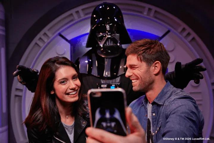 Two smiling guests taking a selfie with Darth Vader