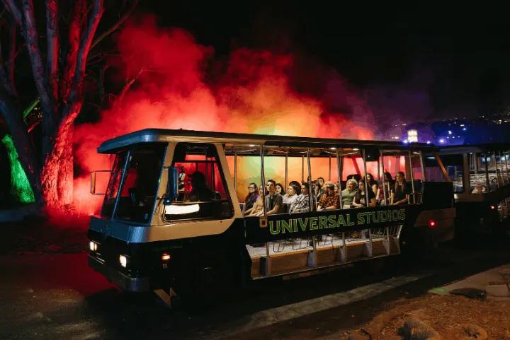 A Universal Studios Terror Tram carrying passengers through a dark setting illuminated by red and green fog
