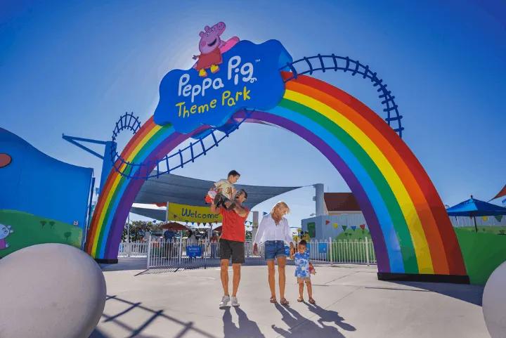 Alt Text: A family walking under the rainbow entrance sign at the Peppa Pig Theme Park