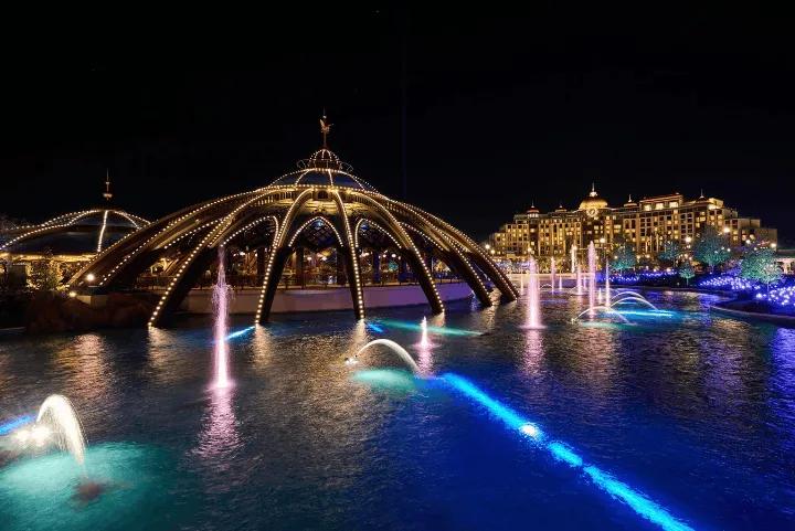 Illuminated fountains and a grand hotel in a theme park at night