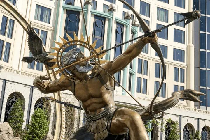 A bronze statue of an archer figure aiming a bow and arrow with a bird companion, situated in front of the ornate hotel facade