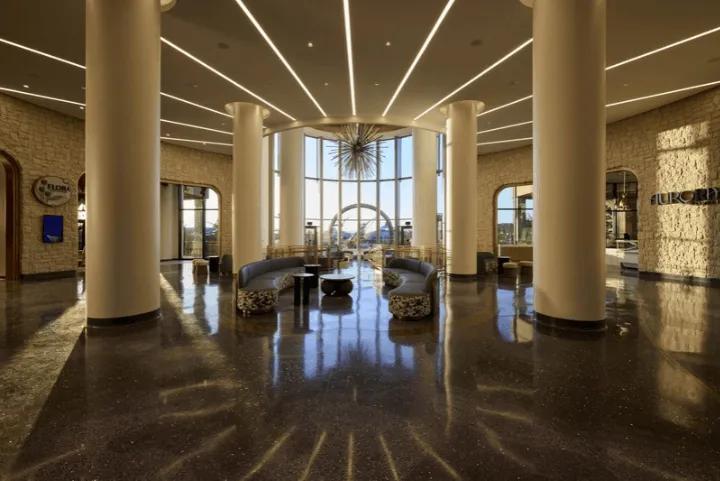 Interior of the spacious, high-ceilinged hotel lobby featuring large support columns, curved seating, and a decorative starburst chandelier
