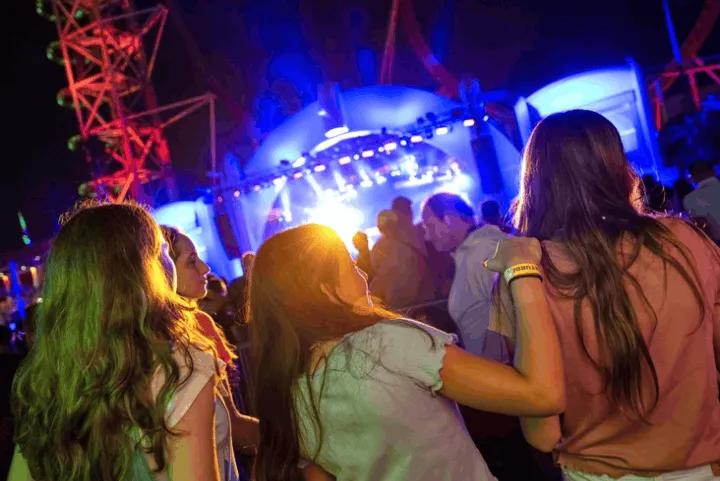 A crowd of people watching a brightly lit live concert stage at night