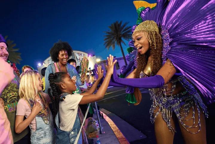 A Mardi Gras parade performer in a purple costume high-fiving a child in the crowd