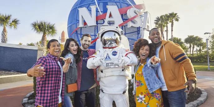 A group of 5 friends posing with someone in an space suit in front of the NASA logo