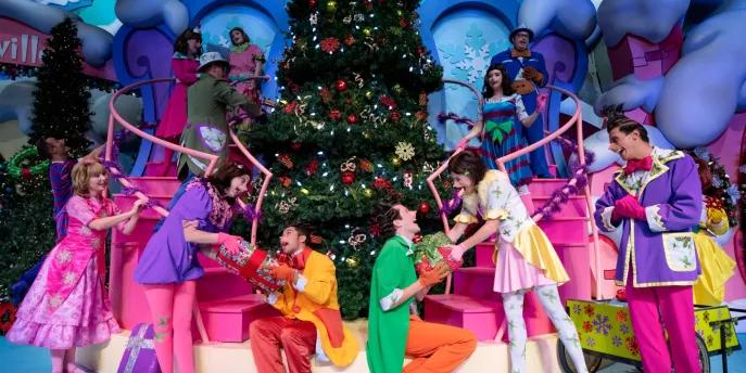 Christmas at Universal Orlando Resort Performers dressed as Whos from the Grinch wearing bright coloured clothes and exchanging gifts in front of a large Christmas tree