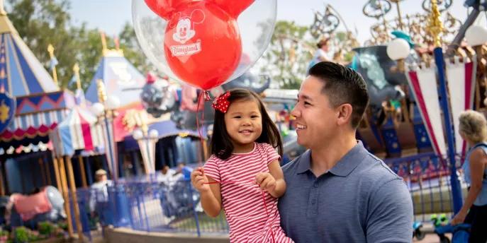 Kids Attractions at Disneyland Resort in California A man holding a young girl who is carrying a balloon standing in front of Dumbo the Flying Elephant
