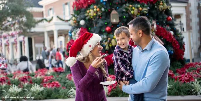 A man holding a small boy who is smiling at a woman eating a cookie and wearing a Santa hat