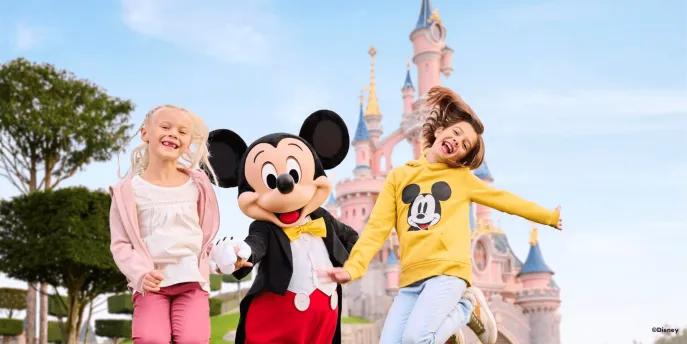 Two young girls jumping with Mickey Mouse in front of the Disneyland Paris castle