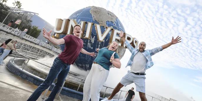 Three people jumping excitedly in front of the Universal Globe