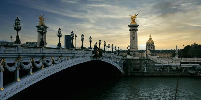 A bridge over the river seine with the sunsetting in the background. there are golden statues on the bridge.