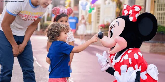 A young boy touching Minnie Mouse on the tip of her nose