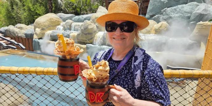 Bubbly Barrel’s DK Crush Float with Mug Woman in theme park holding two barrel themed mugs filled with drinks, whipped cream, sprinkles and more.