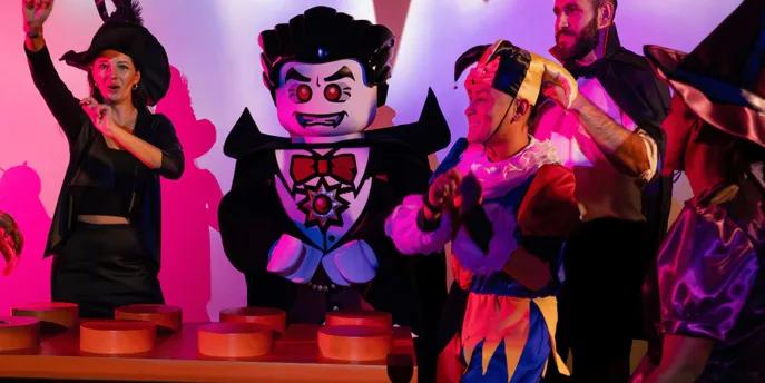 LEGOLAND Dubai Halloween Dracula lego character danging by lego dj deck with kids gethered around wearing halloween costumes.