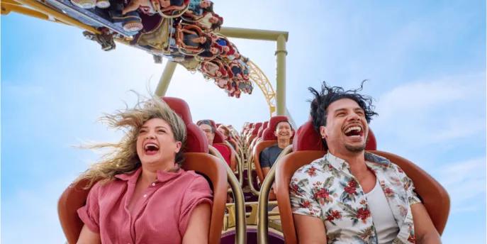 Two adults laughing and screaming with their hair flying while riding a high-speed roller coaster at Universal Orlando Resort, illustrating the kind of thrill ride experience you secure by booking tickets in advance.