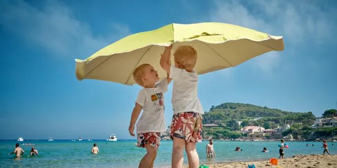 Children playing with beach umbrella on family summer vacation.