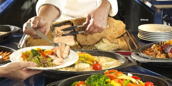 A chef serving fresh salt-crusted salmon and roasted vegetables at a Disneyland Paris buffet.