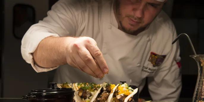 A chef garnishing fresh gourmet tacos on a platter at a Universal Orlando Resort restaurant.