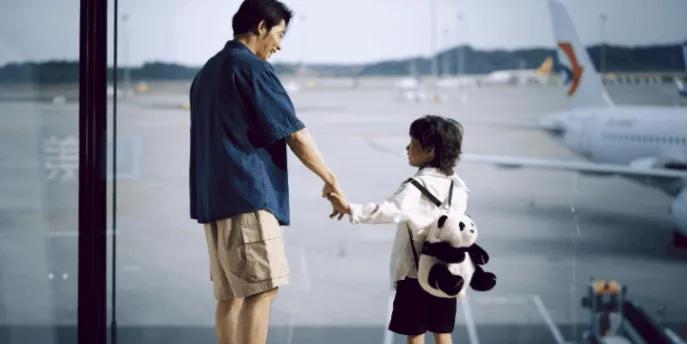 A father and son looking out the window at an airport