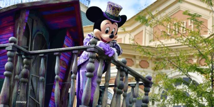 Mickey Mouse in a purple Halloween costume and top hat waving from a balcony at the Disney Halloween Festival