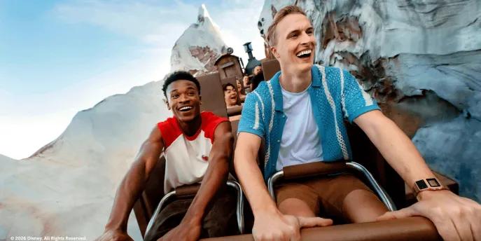 Two young men laughing as they ride the Expedition Everest roller coaster train through snow-covered mountain peaks