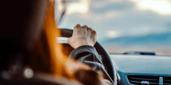 Over-the-shoulder view of a person holding a steering wheel while driving