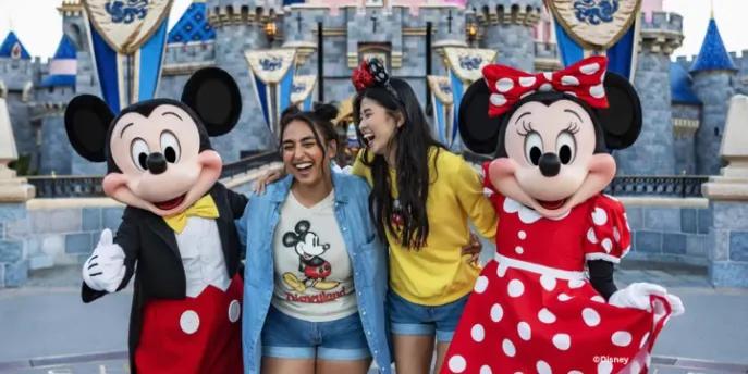 Two friends laughing while posing with Mickey Mouse and Minnie Mouse in front of Sleeping Beauty Castle