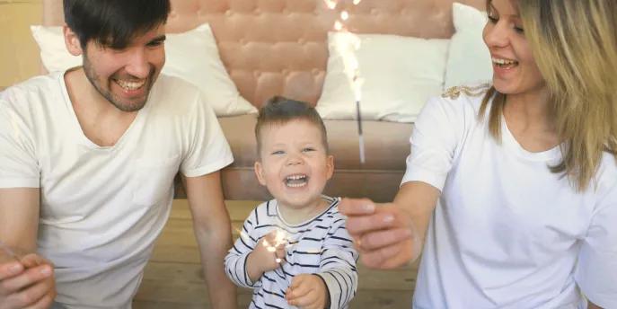 A young family celebrating together at home with sparklers, smiling and laughing