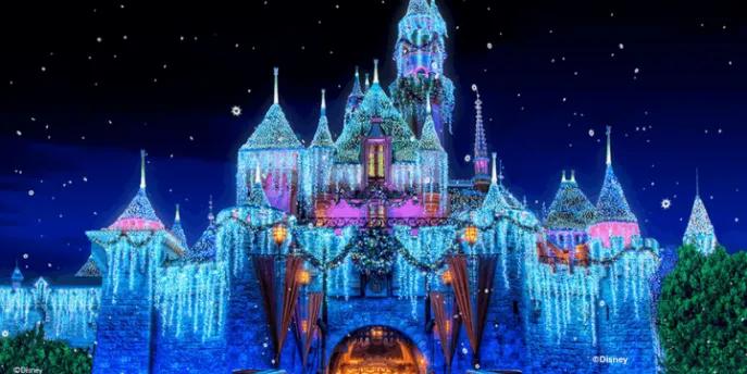 Sleeping Beauty Castle at Disneyland Resort glowing at night with shimmering icicle lights, holiday wreaths, snow-capped turrets, and falling snow effect