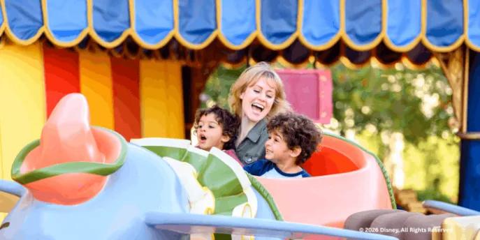 A smiling woman and two young boys riding the Dumbo the Flying Elephant attraction