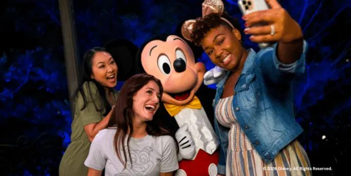 Two guests taking a selfie with Mickey Mouse at night