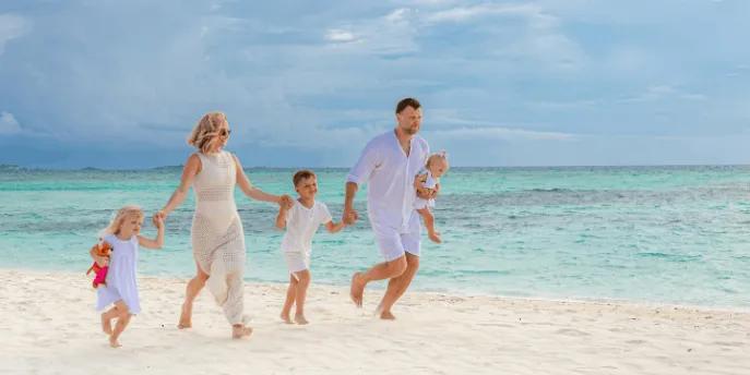 A family dressed in white holding hands and running along a tropical white-sand beach