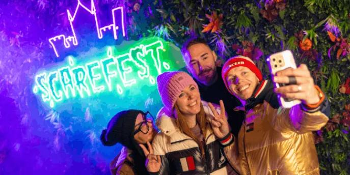 Four friends taking a selfie in front of a glowing neon Scarefest sign