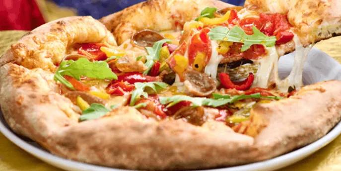 A slice of Harvest Moon pizza with fresh toppings being lifted from a plate at Pizza Moon in Universal Epic Universe