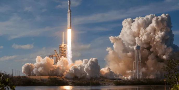 A SpaceX Falcon Heavy rocket launching from the pad, surrounded by large plumes of exhaust