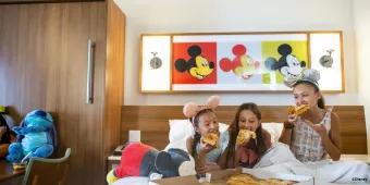 Disney Resort Hotels Three young girls sat on a bed eating pizza from a takeaway pizza box