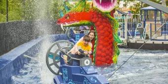 A woman and child getting splashed in a boat ride vehicle in front of a giant Lego sea serpent 