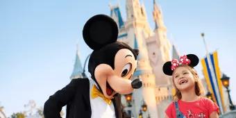 Mickey Mouse walking hand in hand with a young girl in front of Cinderella Castle