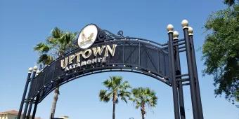 An iron overhead sign for Uptown Altamonte in front of palm trees and a blue sky
