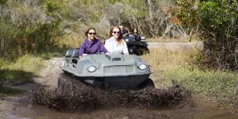 Two people sat side by side in a mucky duck 4x4 vehicle driving into water