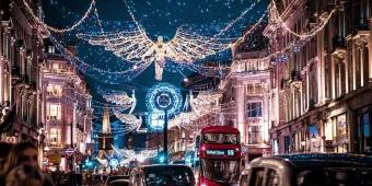 Black taxis and a red London bus driving down Oxford Street underneath the Christmas lights