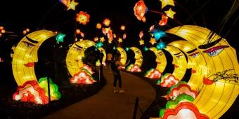A woman standing on a path lined with large crescent moon shaped lanterns and stars