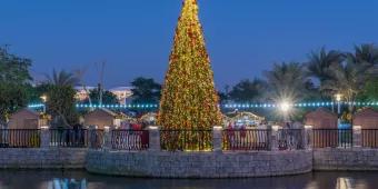 Christmas at Dubai Parks and Resorts A giant lit up Christmas tree next to a river that is reflecting the light