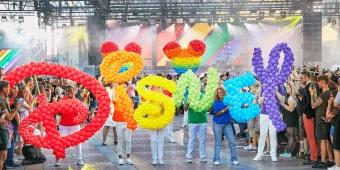People in a parade holding rainbow coloured balloon letters that spell out Disney